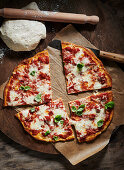 Pizza Margherita on pizza board next to pizza dough and dough roller