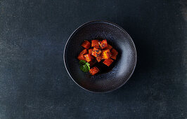 Marinated sweet potato cubes in a black bowl on a dark stone background