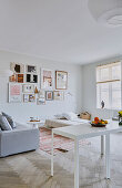 Two white tables as a room divider to a living room with a picture gallery