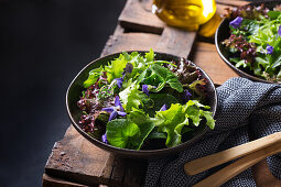 Vegetarian salad with green and red lettuce leaves and edible flowers against jug of oil