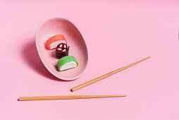 Bunte, süße Sushi, serviert in Keramikschale mit Essstäbchen auf rosa Hintergrund
