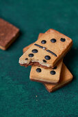 Sweet dominoes shaped cookies with black dots and bitten piece scattered on green surface