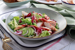 Salad with pieces of chicken wrapped in bacon and avocado, red onion and green lettuce