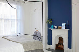 Queen bed with canopy, white floor-to-ceiling built in wardrobe and fireplace against blue wall in bedroom