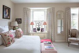 Queen bed and upholstered chest at the end of the bed in a light room with bay window