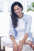 Dark-haired woman in a white top, light blue shirt and white trousers