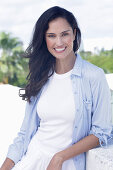 Dark-haired woman in a white top, light blue shirt and white trousers