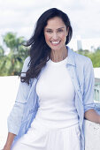 Dark-haired woman in a white top, light blue shirt and white trousers