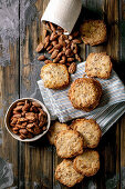 Bowl of glazed honey roasted almond nuts and square shortbread sugar cookies on dark wooden table