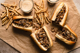 Cheesesteaks and fries on parchment paper with glasses of dark beer
