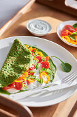 Spinach creppe with tomato and pepper slices and sour cream served on white dishware
