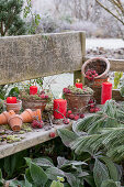 Weihnachtlich dekorierter Gartenbank mit Tontöpfen, roten Kerzen und Zieräpfeln