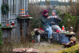 Man and woman with mulled wine and Christmas cookies sitting on a bench in garden