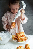 A little girl preparing spiral wafer rolls with a cream filling