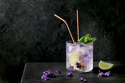 Glass of lemonade soda cocktail with violets flower ice and lime