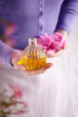 Woman holding flacon with aroma oil and a peony blossom