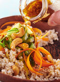 Putting dressing on barley salad with carrots, cucumber, and cashew