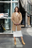 Brunette woman in white knitted dress and beige leather coat