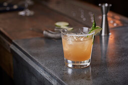 Orange cocktail with a slice of lime and a green chilli