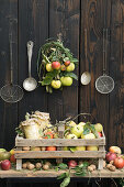 A box of apples and quinces against a wooden wall with kitchen utensils