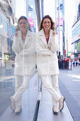 Long-haired woman in white coat and trousers in front of glass wall on the street