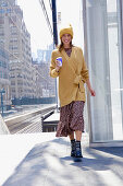 A long-haired woman wearing a knitted hat, a dress and a yellow knitted jumper