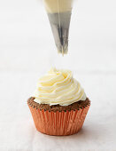 Piping buttercream onto a chai cupcake