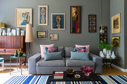Grey upholstered sofa with throw pillows, various tables with vase collections and artwork on grey wall