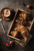 Croissants in a wooden tray with a cup of coffee and fresh berries on a wooden table