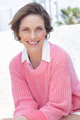 Frau in pinkfarbenem Pullover und weißem Hemd am Strand