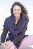 Long-haired woman in a dark coat with a sweater over her shoulders on the beach