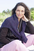 Long-haired woman in a dark coat with a sweater over her shoulders on the beach