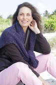 Long-haired woman in a dark coat with a sweater over her shoulders on the beach