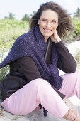 Long-haired woman in a dark coat with a sweater over her shoulders on the beach