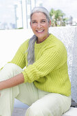 Gray-haired woman in a green-yellow knit sweater and light-colored trousers