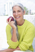 Grauhaarige Frau mit einem Apfel in grüngelbem Strickpullover