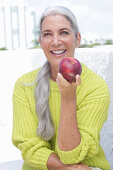 Gray-haired woman with an apple in a green and yellow knit sweater