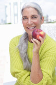 Gray-haired woman with an apple in a green and yellow knit sweater