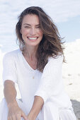 Happy, long-haired woman in white jumper and white trousers on the beach