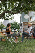 Couple sitting under tree with lanterns in front of extended site trailer