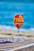 A glass of rosé wine garnished with redcurrants on a table by the sea