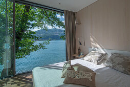 Queen sized bed in bedroom with open, floor-to-ceiling sliding door and lake view