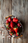 Frische Erdbeeren in Drahtkörbchen auf Holzuntergrund