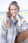 Young blonde woman in checked coat and suede trousers by the sea