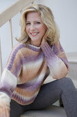 Mature blonde woman in knitted jumper with colour gradient and grey leggings