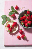 Fresh strawberries with strawberry leaves on a pink background