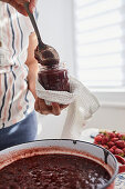 Pouring hot strawberry jam in a jar