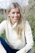 Junge blonde Frau in weißem Rollkragenpullover und Jeans in der Natur