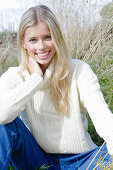 Junge blonde Frau in weißem Rollkragenpullover und Jeans in der Natur