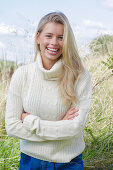 Junge blonde Frau in weißem Rollkragenpullover und Jeans in der Natur